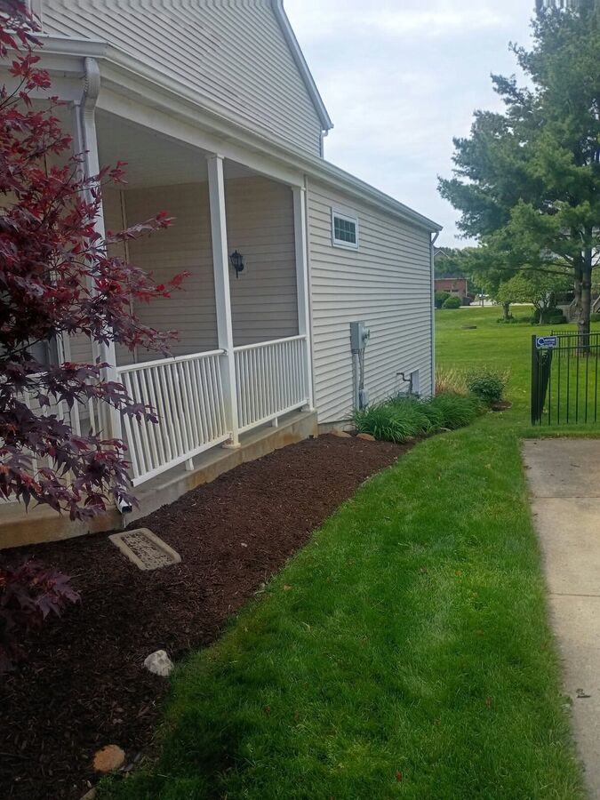 Side yard with fresh dark mulch along the house foundation, hostas near the meter, and a mowed lawn.